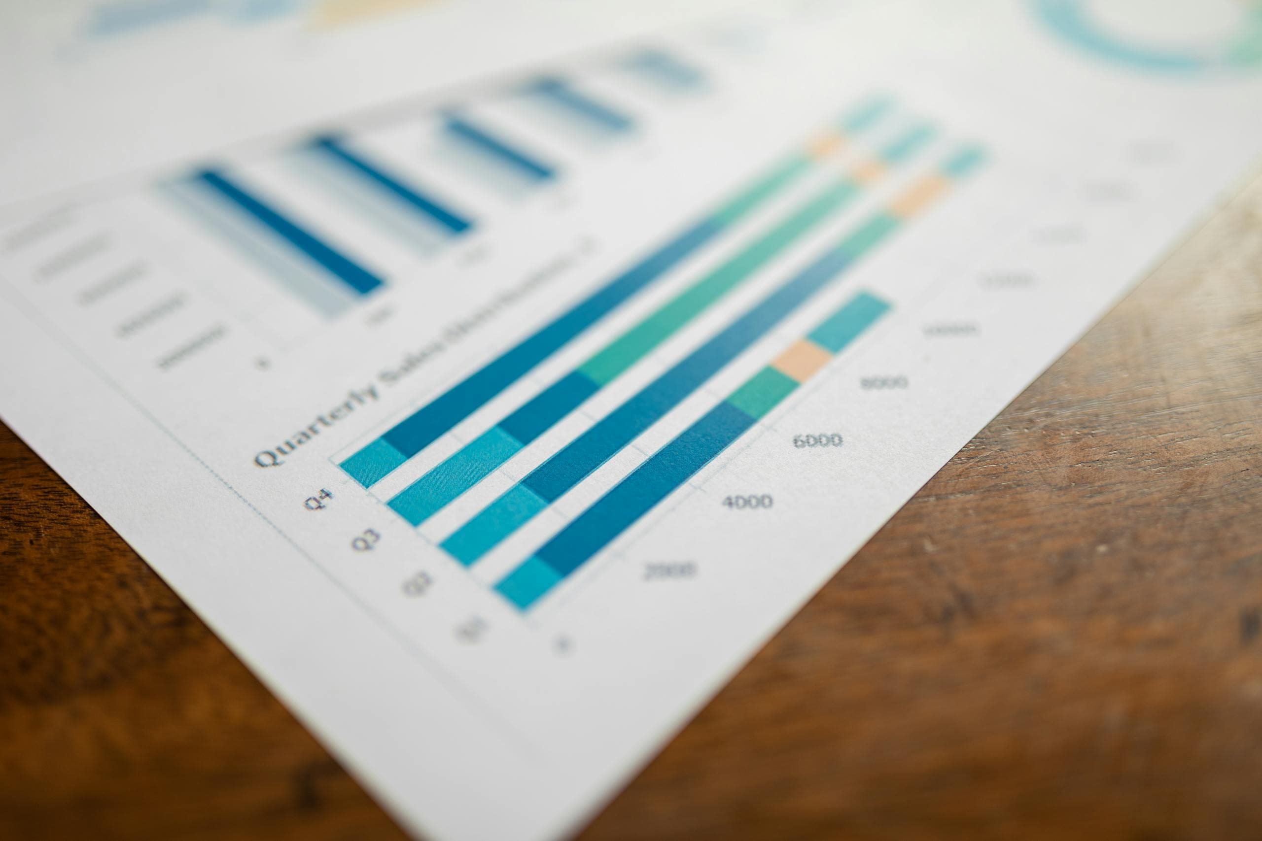 Close-up of a printed quarterly bar chart report on a wooden desk, with blue and green data bars in soft focus.